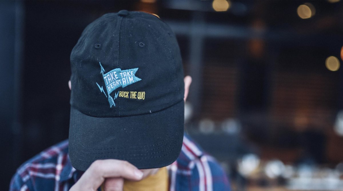 Man wearing black cap with TAKE HEART TAKE AIM and BUCK THE QUO embroidered