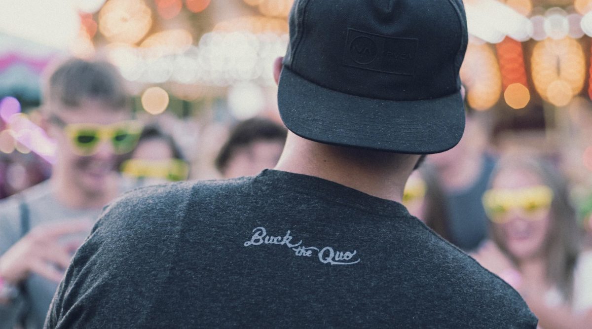 Man with backwards cap and black tee with small Buck the Quo logo on back