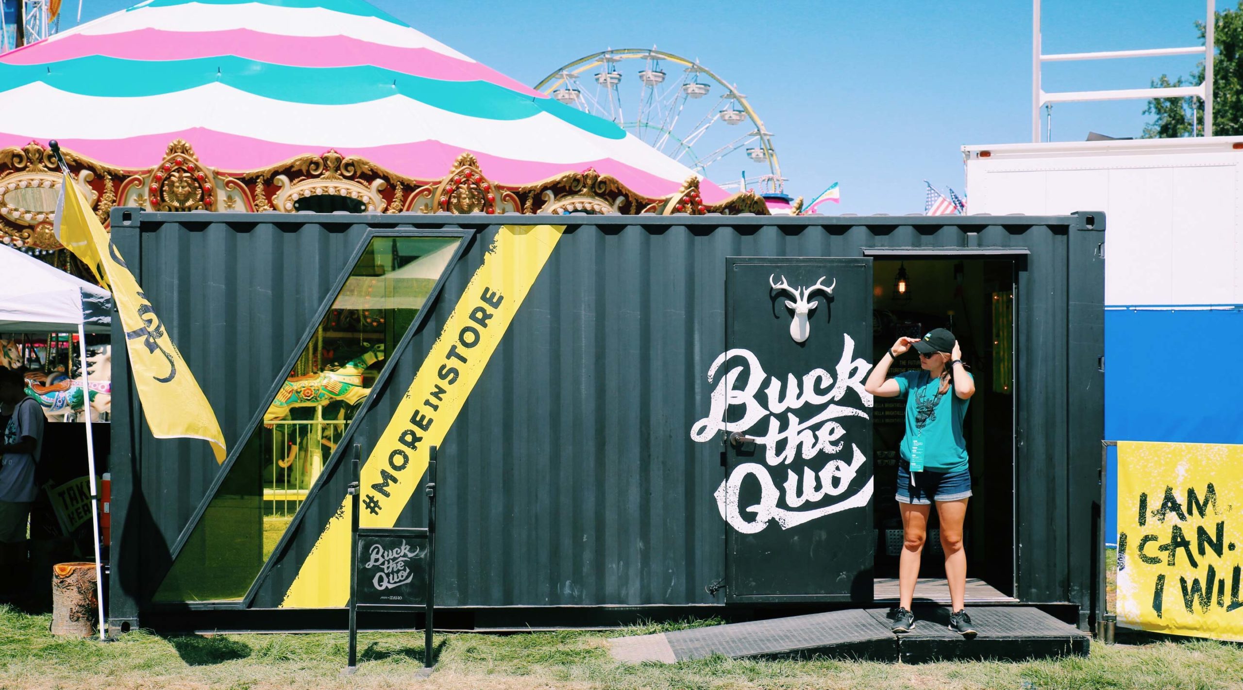 Front of BTQ shipping container with pink tent and ferris wheel in background